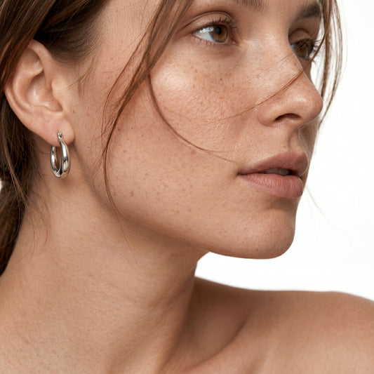 A close-up portrait focusing on a polished sterling silver tapered hoop earring worn by a model with a clean, natural look. The earring features a classic thick-to-thin design, perfect for everyday minimalist style.
