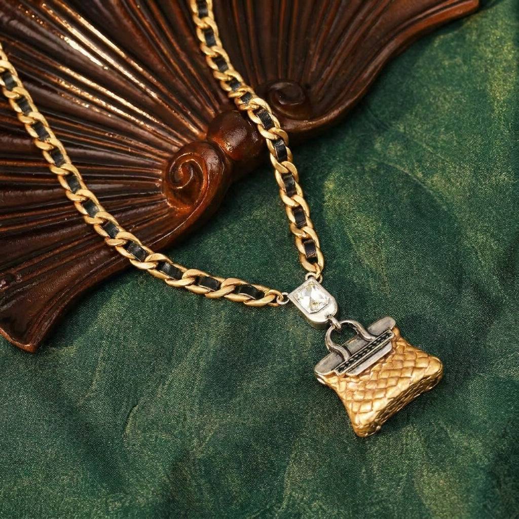 Full layout of the vintage luxury handbag pendant necklace on a rich dark green fabric background with an antique fan decoration.
