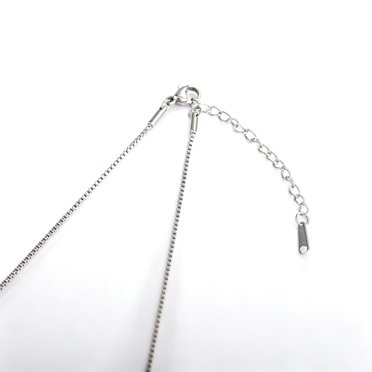 Close-up view of a silver-tone lobster clasp, extender chain, and tag on a box chain.