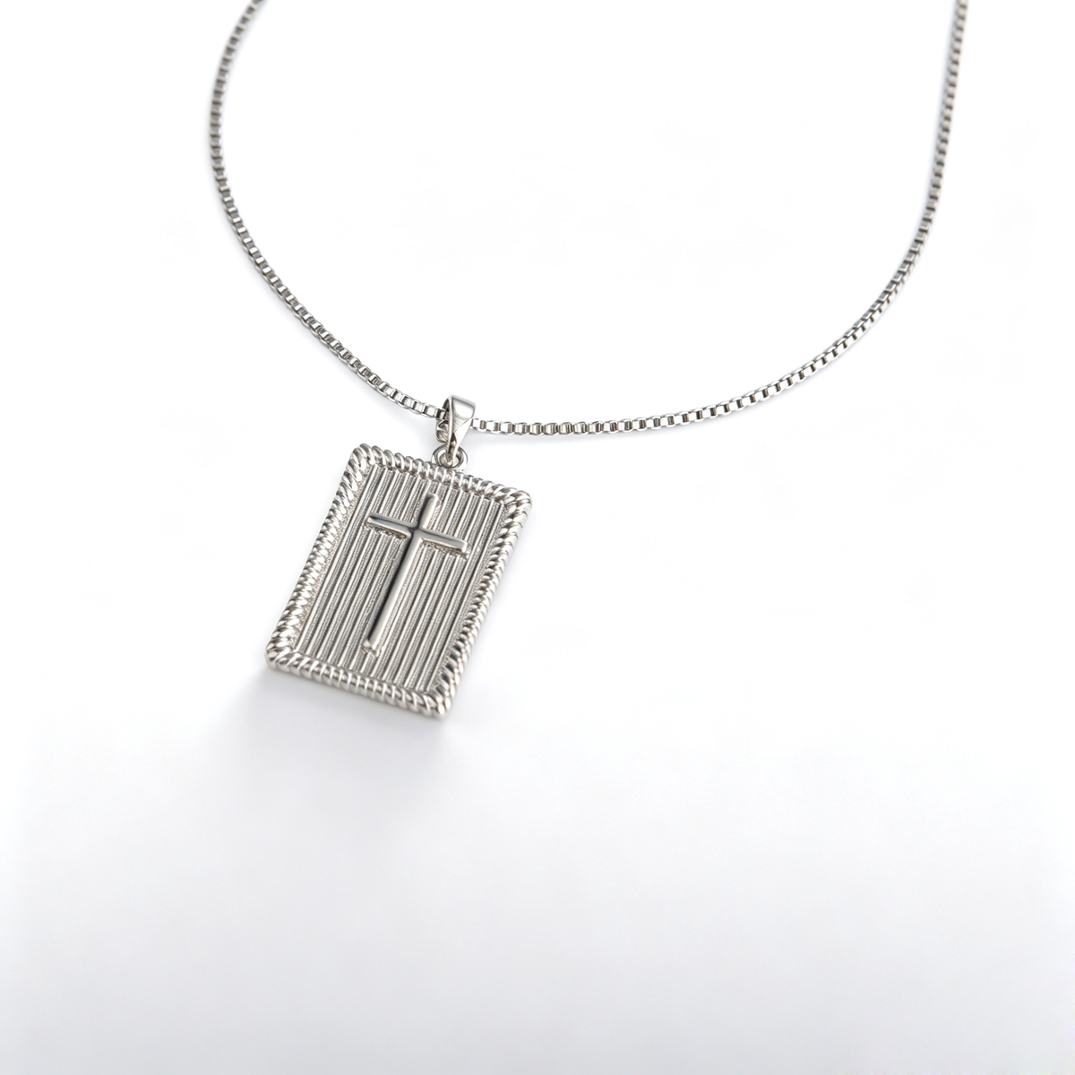 Angled close-up of a textured rectangular cross pendant showing rope-edge details and chain bail.