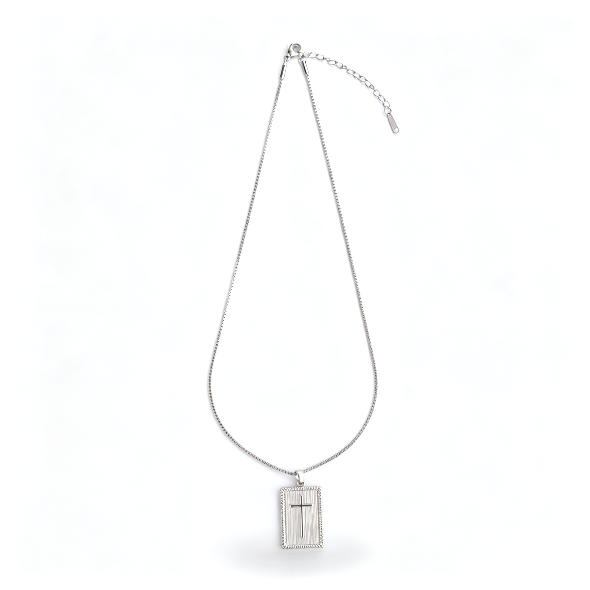 Full length view of a silver-tone rectangular cross pendant necklace laid out on a white surface.