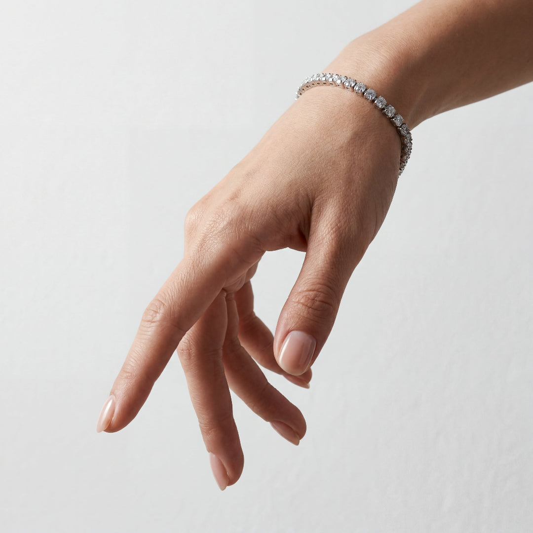 Close-up of a high-polished round cut diamond tennis bracelet on a woman's hand against a white background.