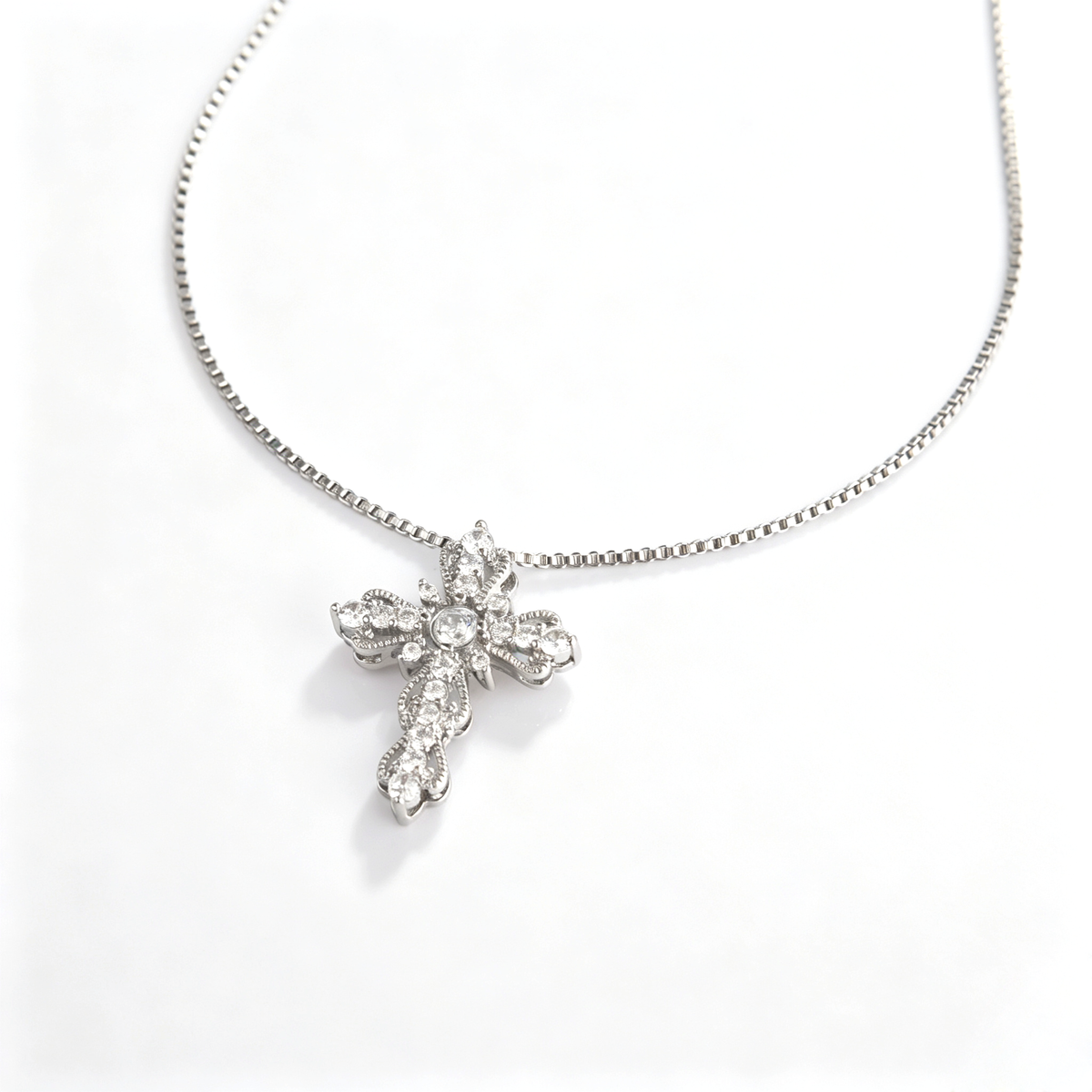 Angled close-up view of an ornate floral scalloped cross pendant with sparkling clear stones.