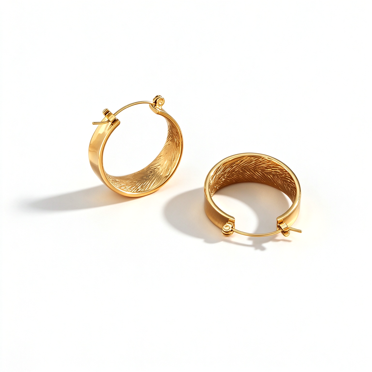 A pair of oval hoop earrings shown at an angle, highlighting the textured inner surface and hinged closures