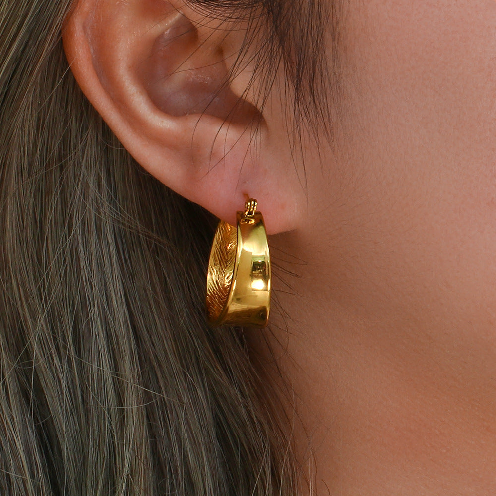 Gold-tone oval hoop earring worn on the ear, showing its curved profile and textured inner detail