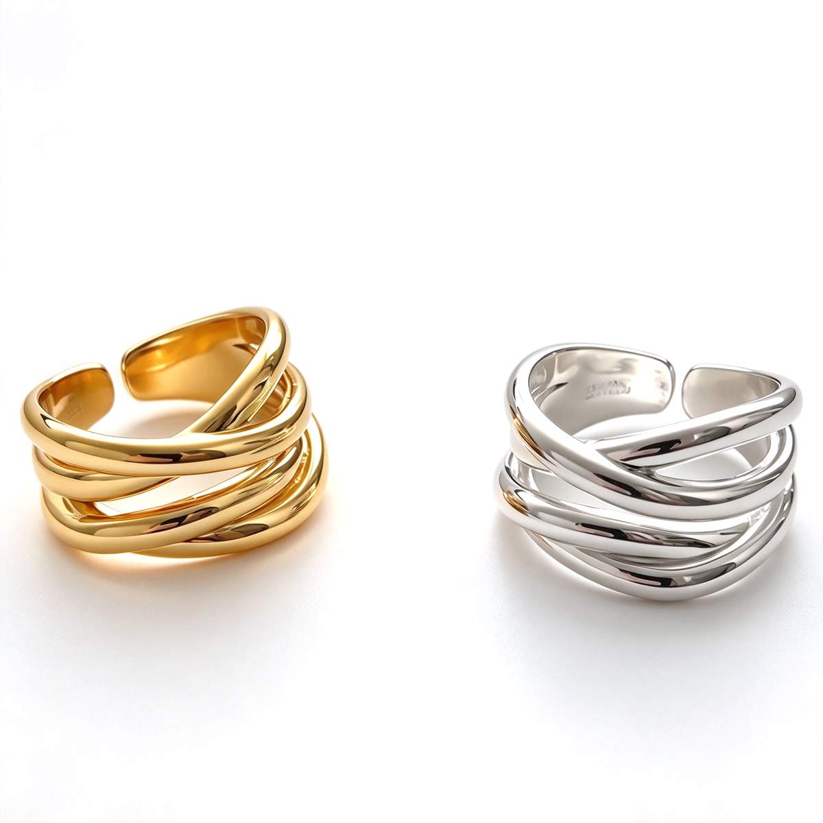Gold-tone and silver-tone sculptural crossover rings displayed together on a white background