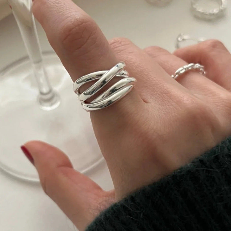 Silver-tone sculptural crossover ring with overlapping curved bands shown on a white background
