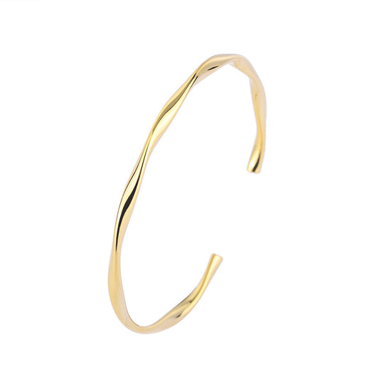 Sculptural open cuff bracelet with a flowing curved shape in gold tone