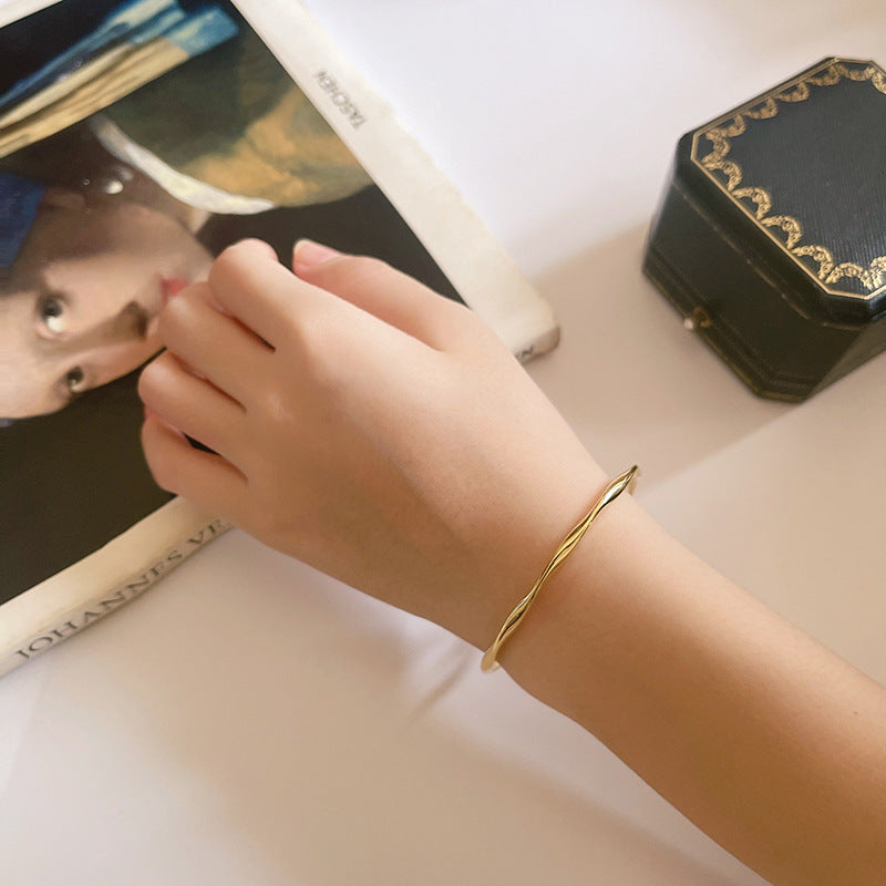 Gold tone open cuff bracelet worn on the wrist in a natural lifestyle setting
