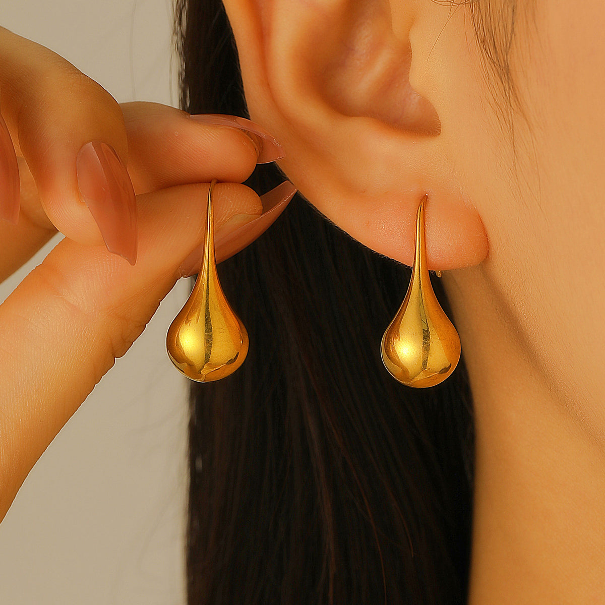 Close-up of silver-tone teardrop dangle earrings worn on an ear, highlighting their curved silhouette.
