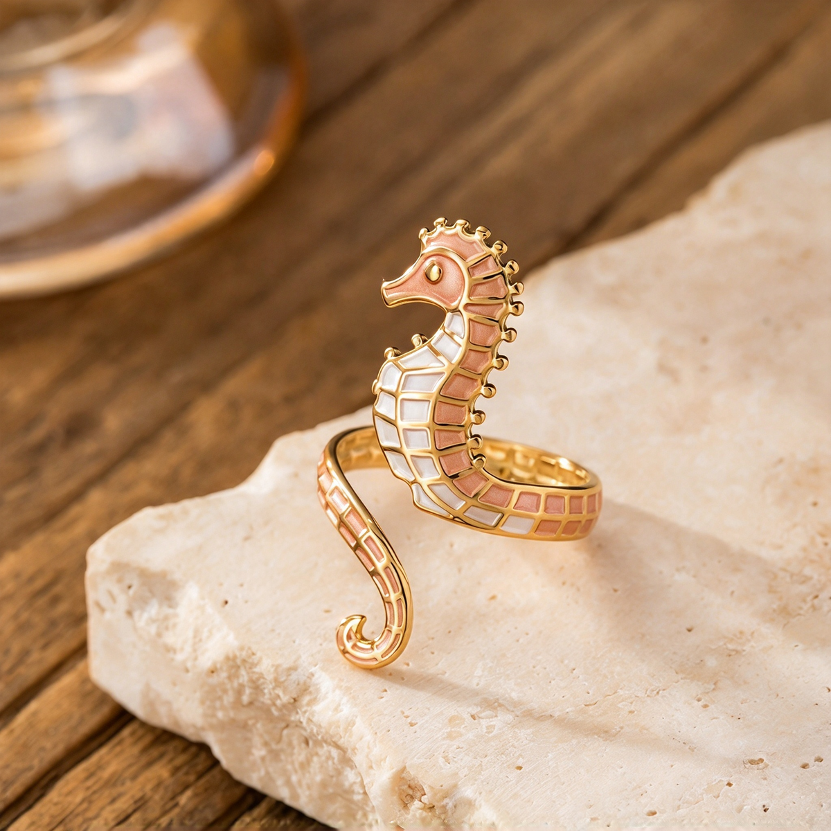 Gold-tone seahorse ring with pink and cream-colored sections displayed on a pale stone surface