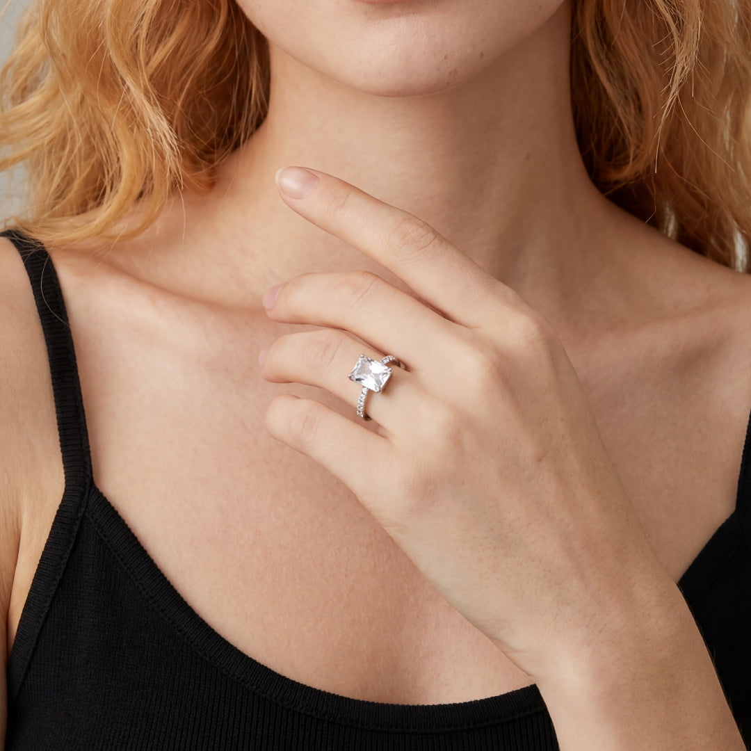 Close-up of a square radiant cut engagement ring on model's hand.