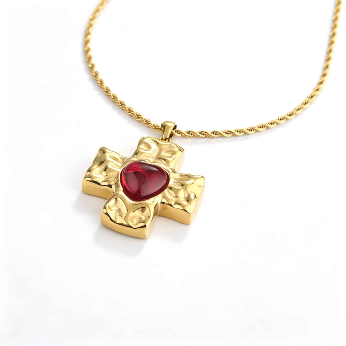 Angled view of an 18k gold-plated hammered cross pendant centered with a ruby red heart CZ stone.