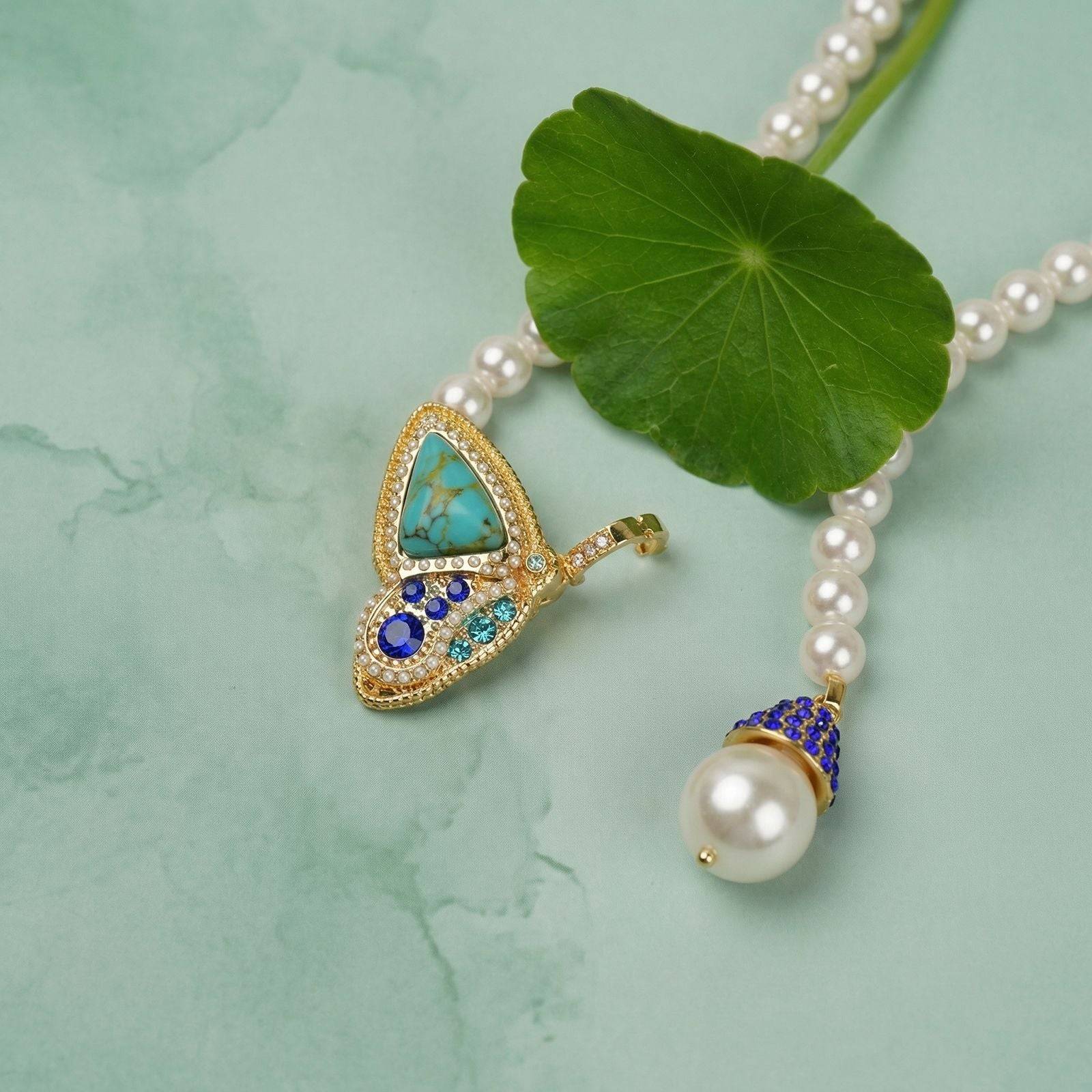 Micro close-up of the heavy gold-plated copper butterfly element inlaid with natural turquoise matrix texture, blue rhinestones, and a crystal cap pearl.