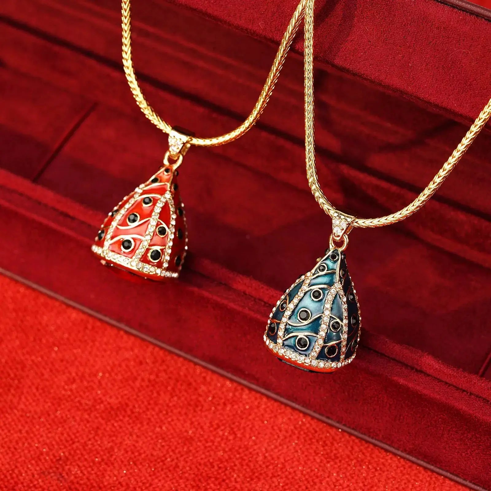 Royal emerald green and ruby red vintage French enamel egg pendant necklaces on a premium crimson velvet jewelry display.