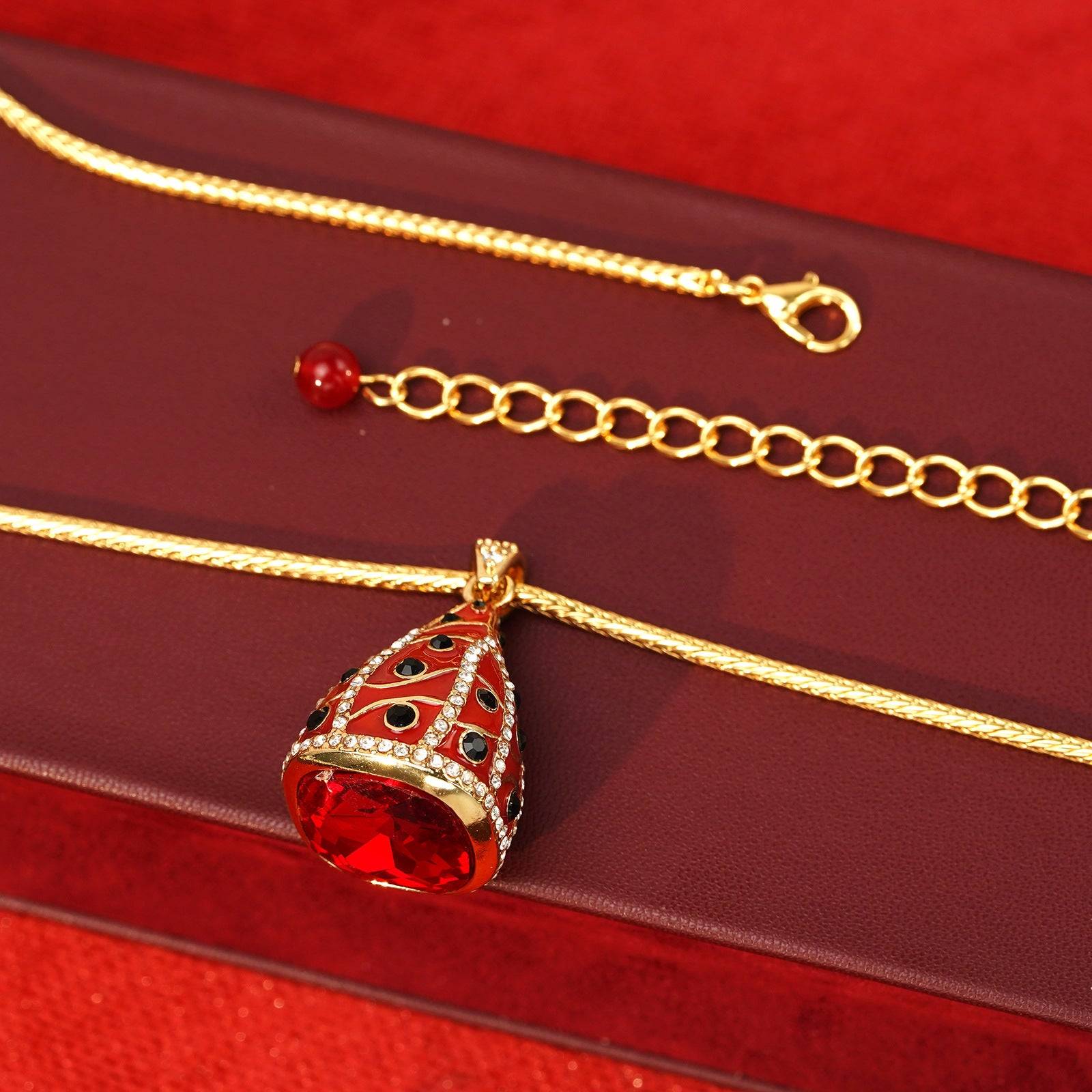 Details of the high-shine gold wheat chain and secure lobster clasp with a coordinating red crystal bead dangle.