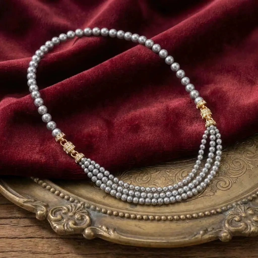 Sophisticated grey multi-strand faux pearl necklace in a classic French baroque style, resting on a textured dark red velvet cloth.