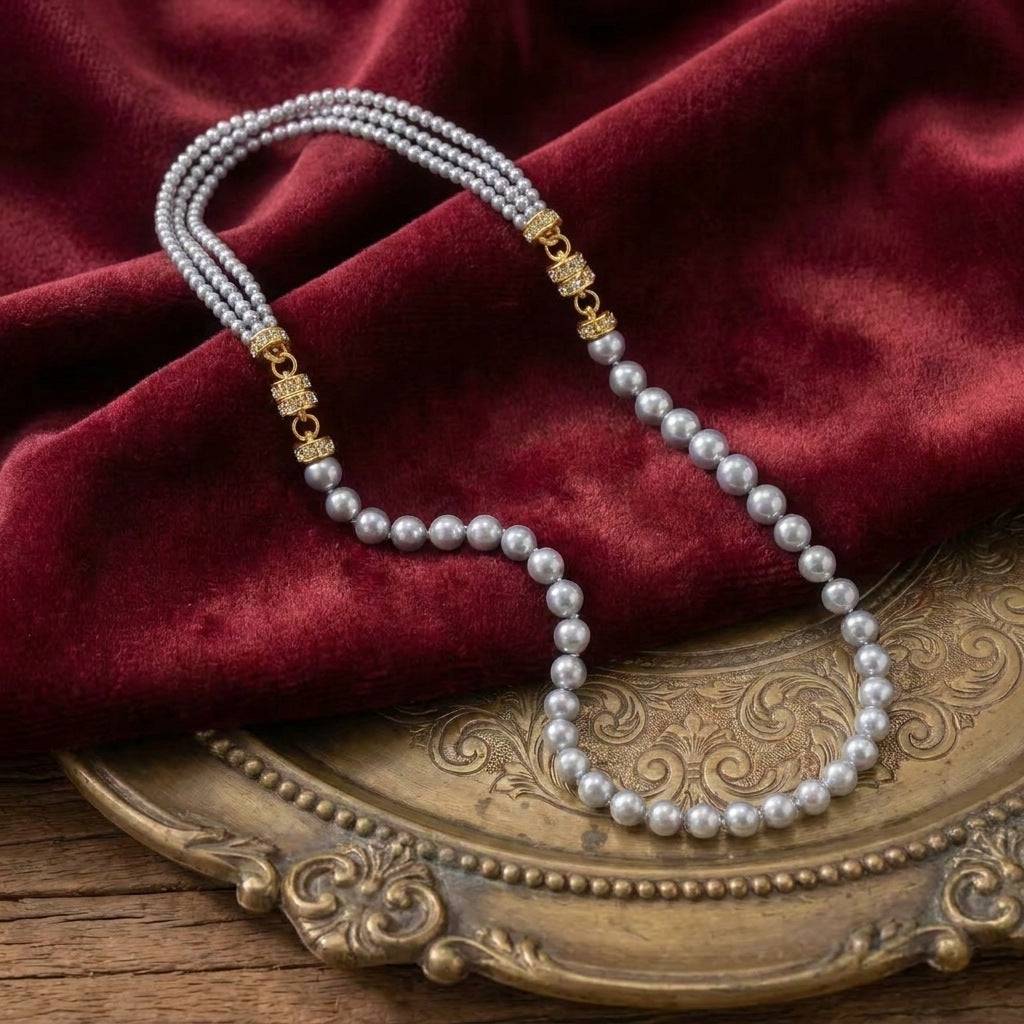 Elegant draping of the grey multi-layer vintage pearl necklace on an ornate golden tray, highlighting its metallic luster and rhinestone detailing.