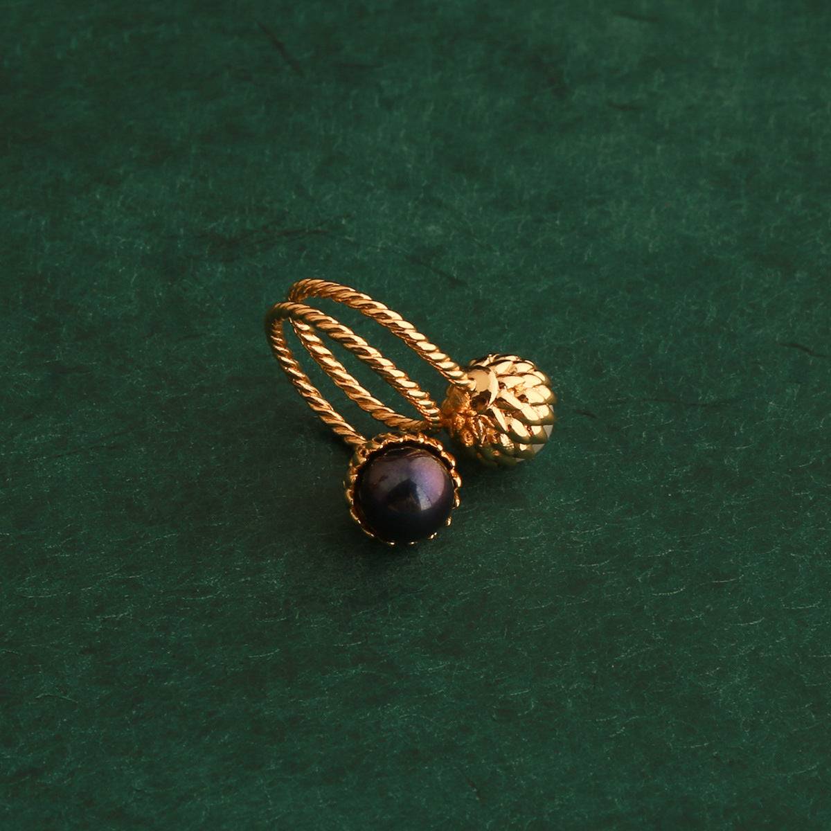 Top view of Ever P. vintage gold pinecone two-tone pearl bypass ring featuring a dark black-purple pearl on a textured dark green background.