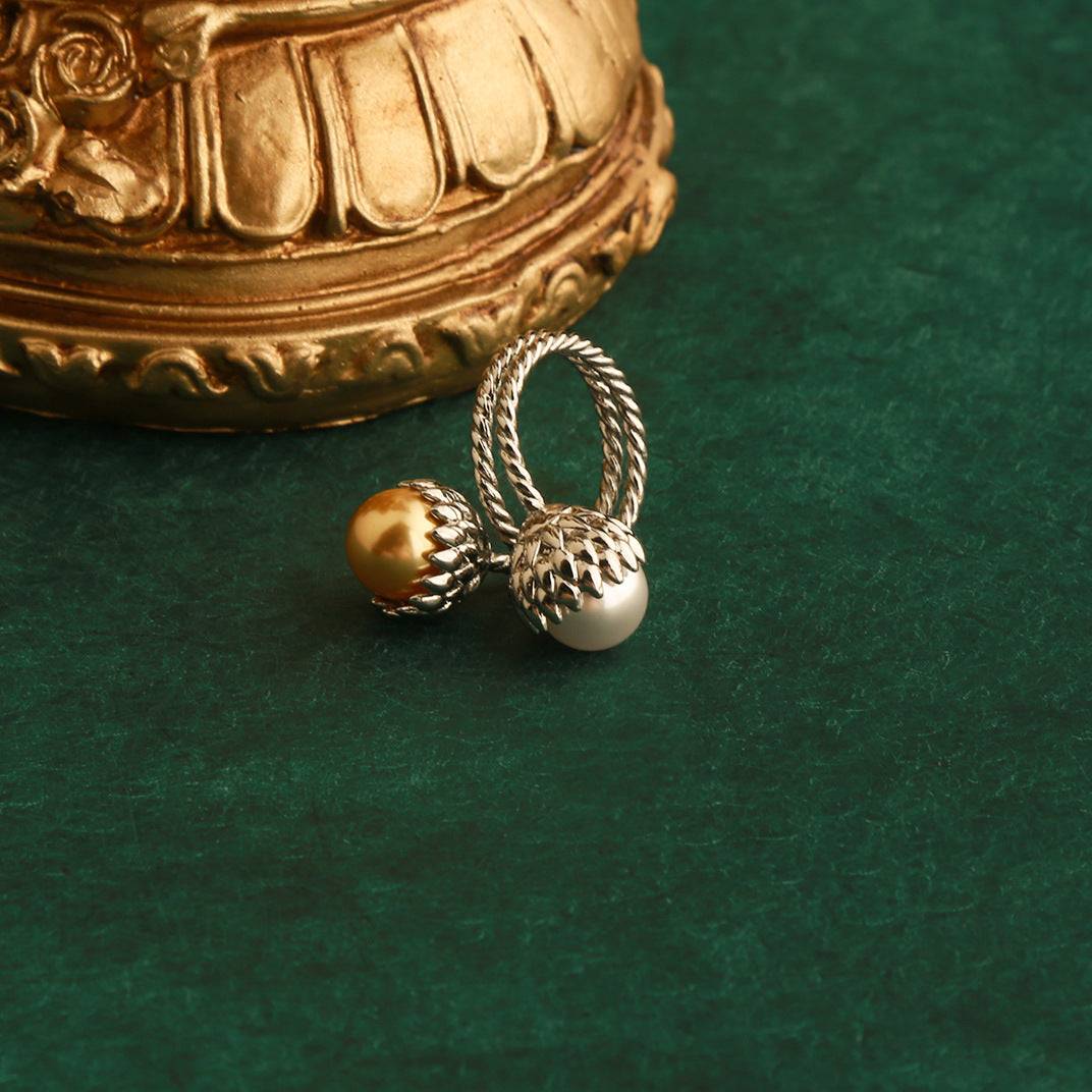 Silver-plated pinecone Toi et Moi ring featuring a honey-gold pearl and white pearl, resting next to a baroque gold ornament.