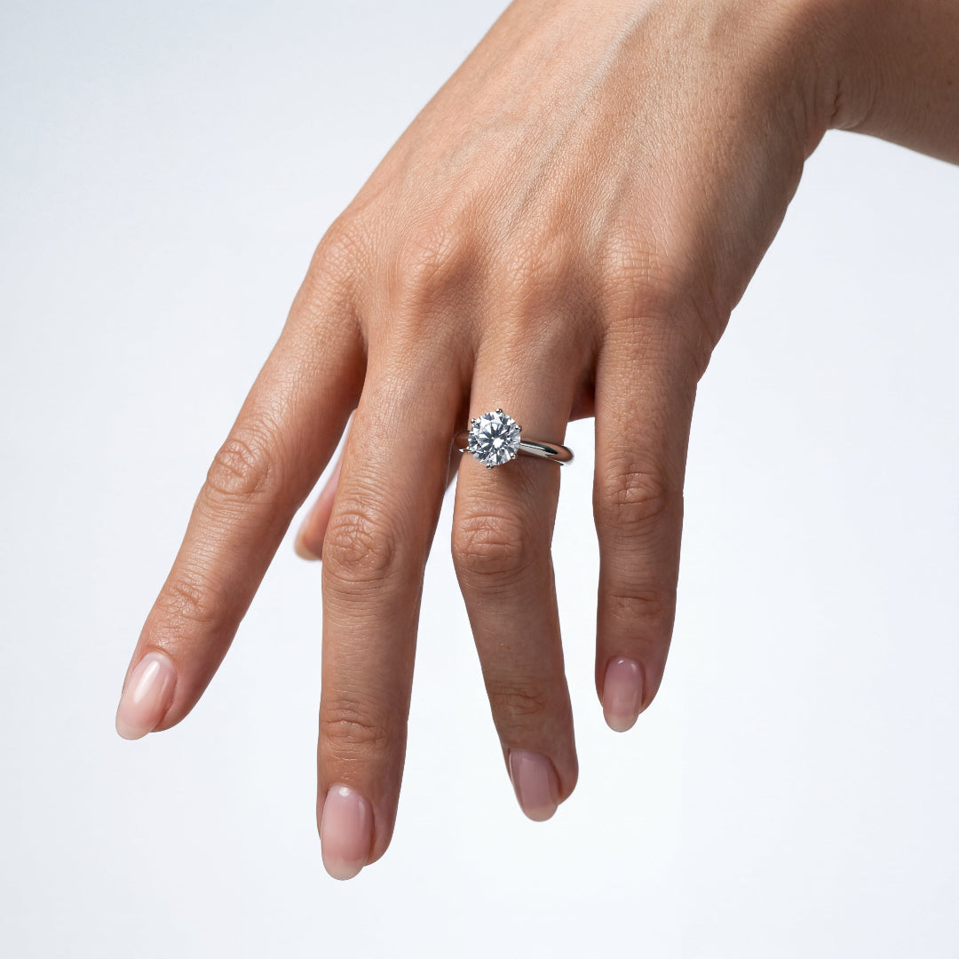 A dangling woman's hand showcasing a classic four-prong solitaire round diamond ring.