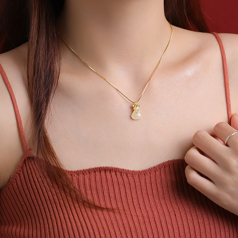 Money bag pendant necklace worn with a rust-colored top, shown at the center of the neckline.
