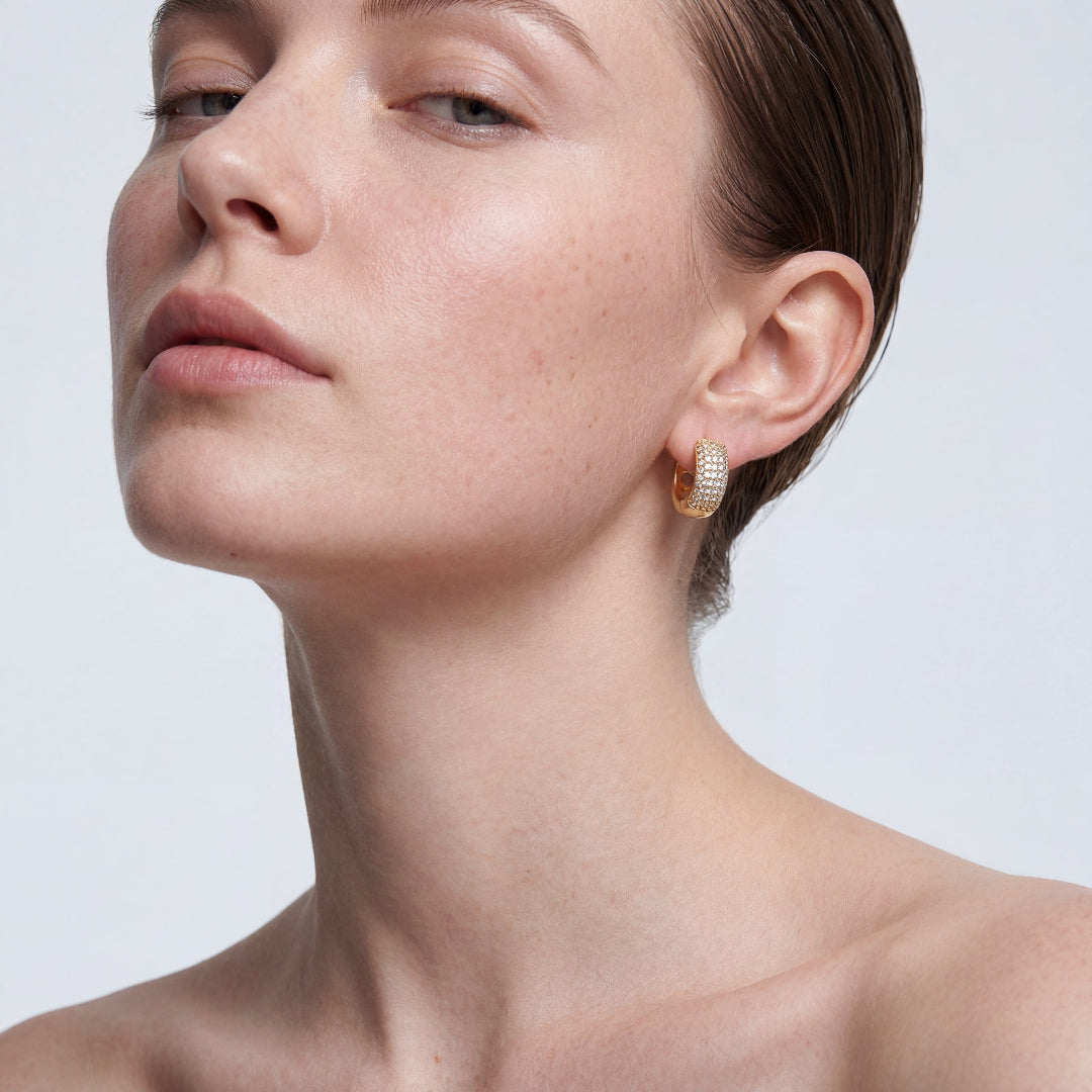 High-angle portrait of a model showcasing a thick 18k gold plated hoop earring featuring rows of brilliant pave crystals. Minimalist aesthetic highlighting elegant ear jewelry.